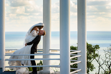 Image showing The newlyweds kiss in a beautiful picturesque gazebo against the backdrop of the sea