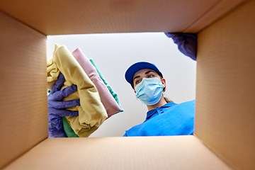 Image showing woman in mask packing clothes to parcel box