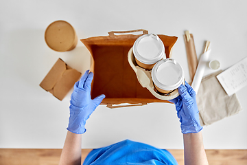 Image showing delivery woman in gloves packing food and drinks