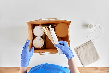 Image showing delivery woman in gloves packing food and drinks