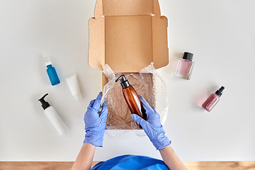 Image showing hands in gloves packing parcel box with cosmetics