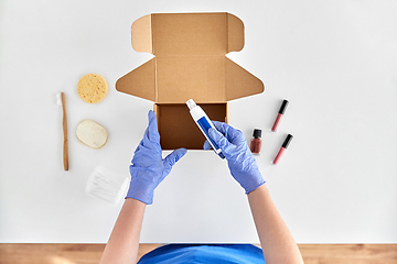 Image showing hands in gloves packing parcel box with cosmetics