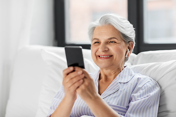 Image showing senior woman with smartphone and earphones in bed