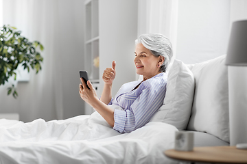 Image showing senior woman with phone having video call in bed