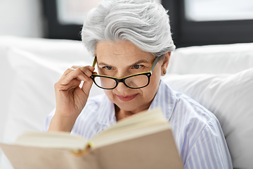 Image showing old woman in glasses reading book in bed at home