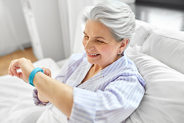 Image showing happy old woman with health tracker sitting in bed