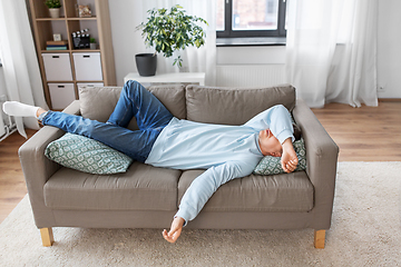 Image showing bored or lazy young man lying on sofa at home