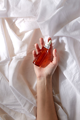 Image showing female hand holding bottle of serum on white sheet