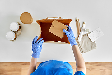 Image showing delivery woman in gloves packing food and drinks