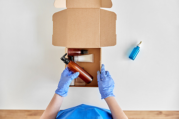 Image showing hands in gloves packing parcel box with cosmetics