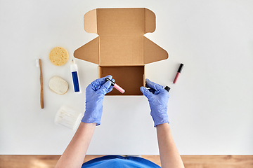 Image showing hands in gloves packing parcel box with cosmetics