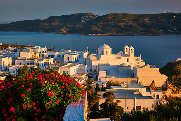 Image showing View of Plaka village on Milos island over red geranium flowers on sunset in Greece
