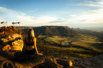 Image showing Female sitting high on a cliff look out over sunlit valley