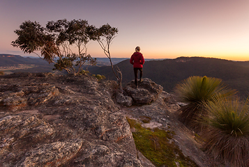 Image showing Woman standing on rocky mountain  ledge at sunset