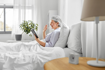 Image showing old woman with tablet pc having video call in bed