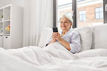 Image showing happy senior woman using smartphone in bed at home