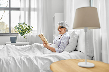 Image showing old woman in glasses reading book in bed at home