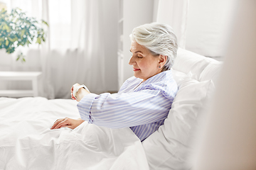 Image showing happy senior woman sitting in bed at home bedroom