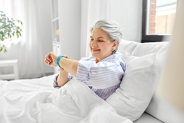 Image showing happy old woman with health tracker sitting in bed