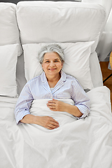 Image showing smiling senior woman lying in bed at home bedroom