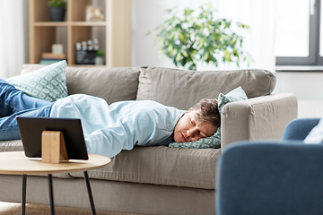 Image showing bored man with tablet pc lying on sofa at home