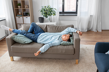 Image showing bored or lazy young man lying on sofa at home