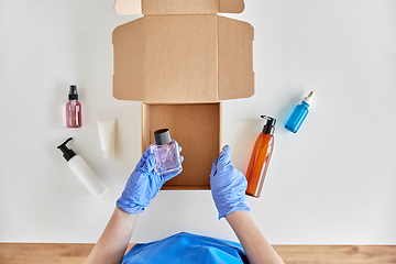 Image showing hands in gloves packing parcel box with cosmetics