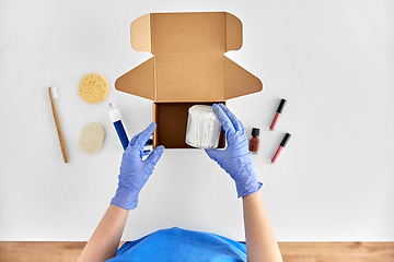 Image showing hands in gloves packing parcel box with cosmetics