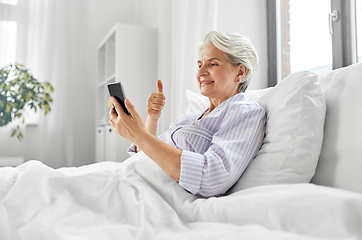 Image showing senior woman with phone having video call in bed