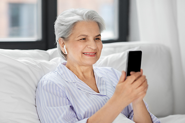 Image showing senior woman with smartphone and earphones in bed