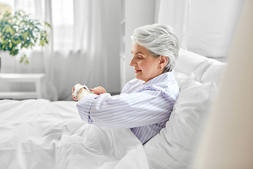 Image showing happy senior woman sitting in bed at home bedroom
