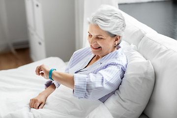 Image showing happy old woman with health tracker sitting in bed