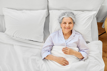 Image showing smiling senior woman lying in bed at home bedroom