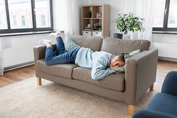 Image showing bored or lazy young man lying on sofa at home