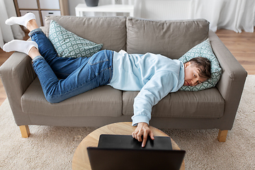 Image showing bored man with laptop lying on sofa at home