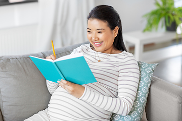 Image showing happy pregnant woman writing to diary at home