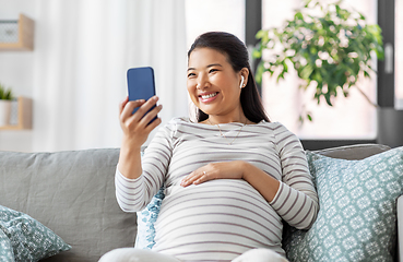 Image showing pregnant woman with phone and earphones at home