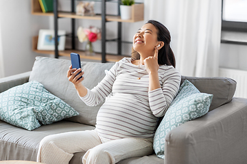 Image showing pregnant woman with phone and earphones at home