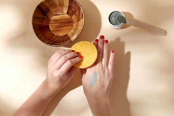 Image showing hands applying blue cosmetic clay mask to skin