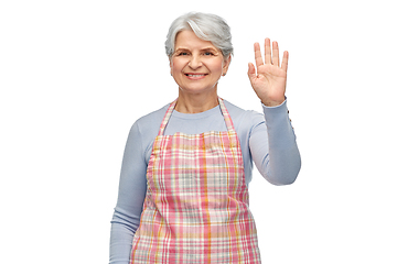 Image showing smiling senior woman in apron waving hand