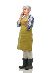 Image showing senior woman in garden apron calling on smartphone