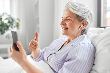 Image showing senior woman with phone having video call in bed