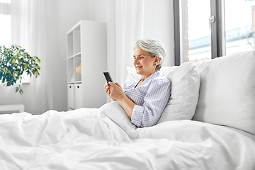 Image showing happy senior woman using smartphone in bed at home