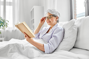 Image showing old woman in glasses reading book in bed at home