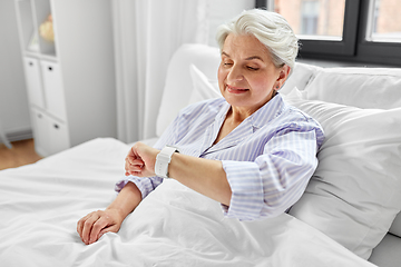 Image showing happy senior woman sitting in bed at home bedroom