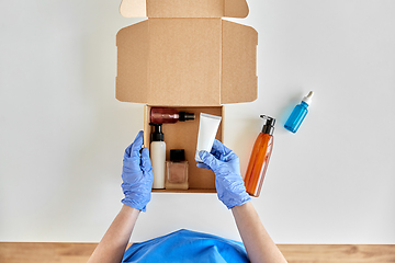 Image showing hands in gloves packing parcel box with cosmetics