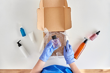 Image showing hands in gloves packing parcel box with cosmetics