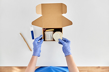 Image showing hands in gloves packing parcel box with cosmetics