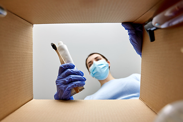 Image showing woman in mask unpacking parcel box with cosmetics