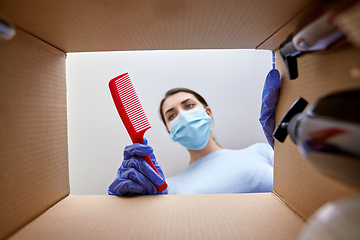 Image showing woman in mask unpacking parcel box with cosmetics